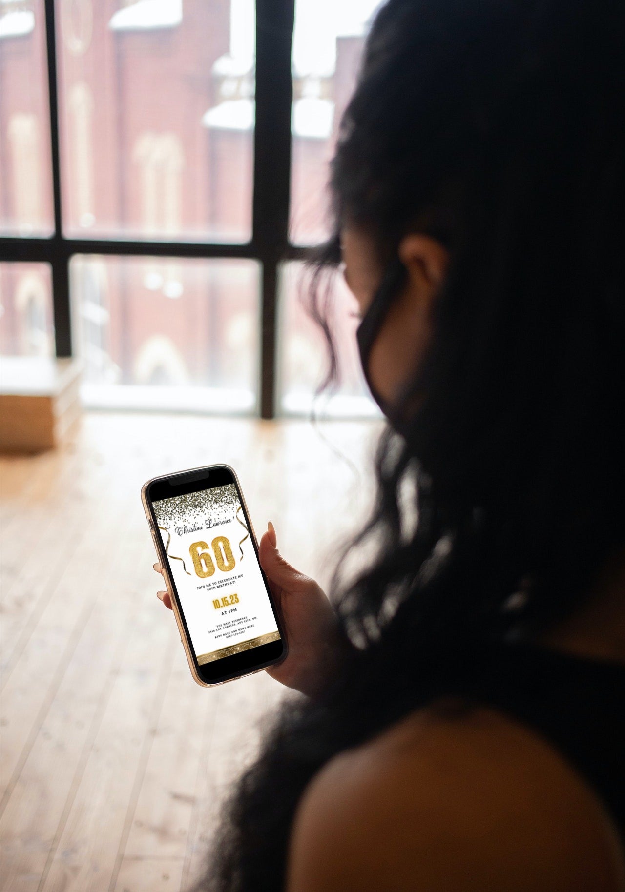 Woman holding a phone displaying a customizable White Gold Confetti 60th Birthday Evite template from URCordiallyInvited, ready for personalization via the Canva app.
