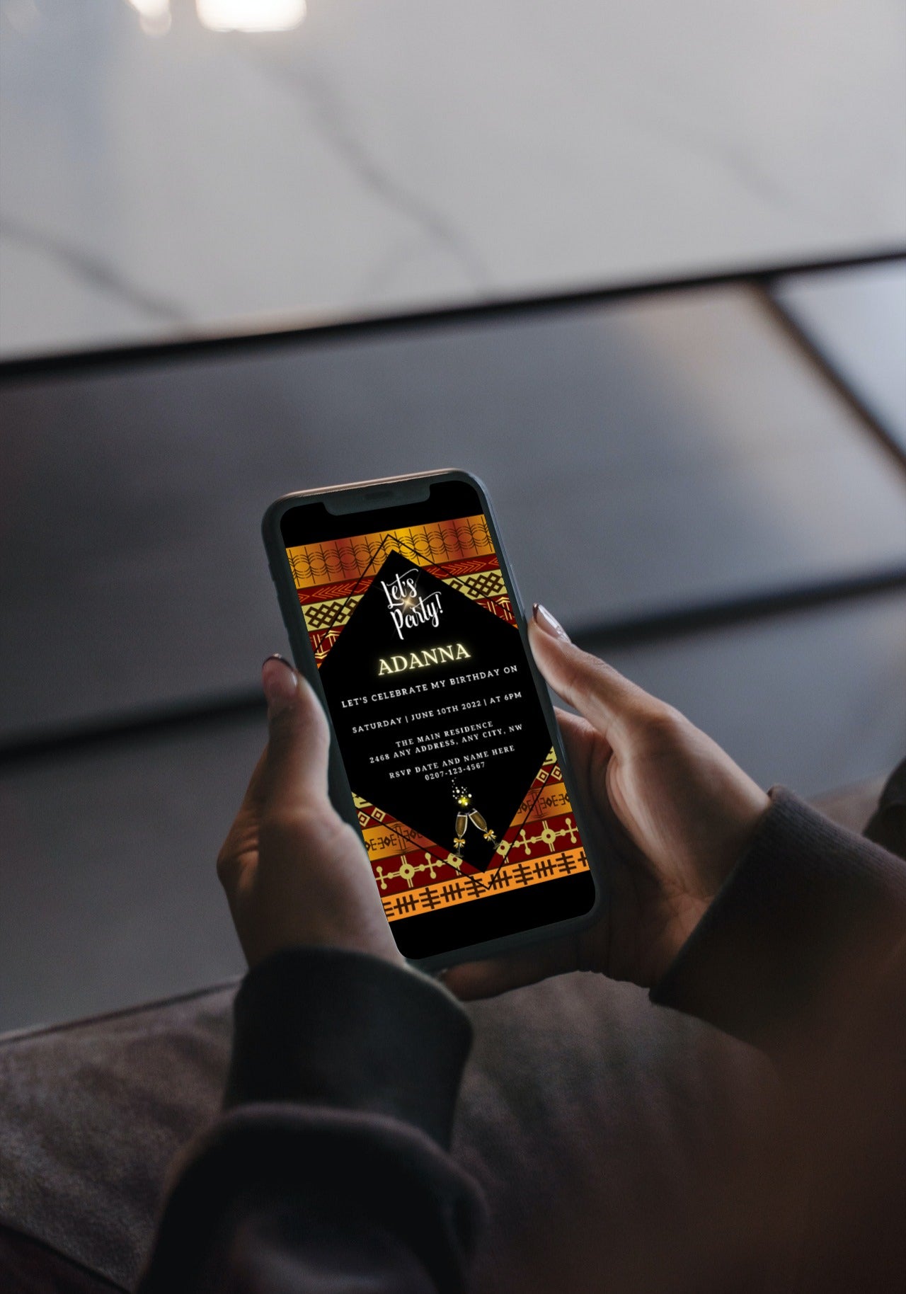 Person holding a phone displaying a Gold Yellow African Ankara Editable Party Evite template from URCordiallyInvited, ready to be customized using Canva.