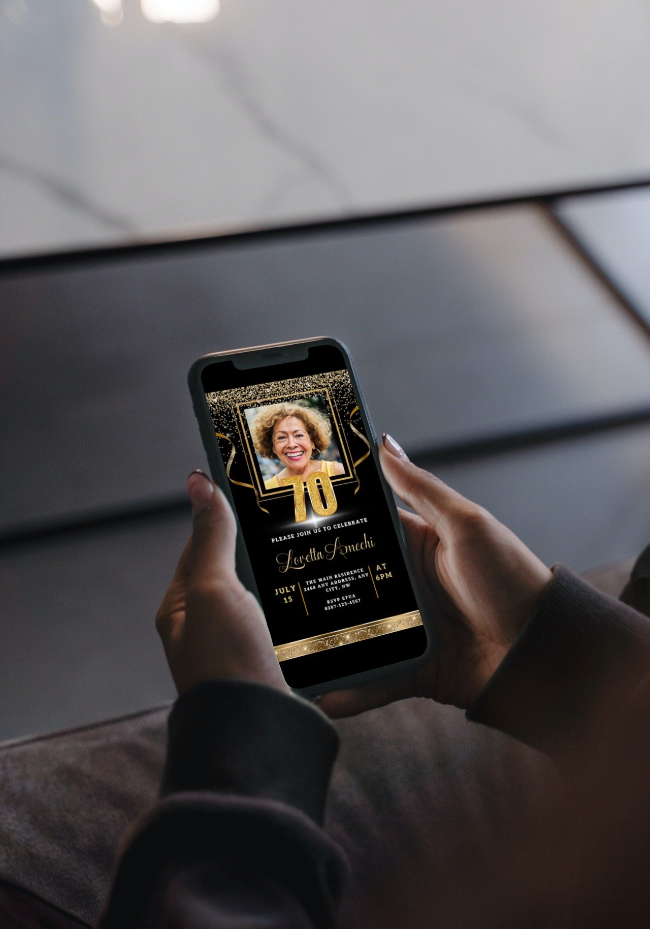 Person holding a smartphone displaying a customizable Digital Black Gold Confetti 70th Birthday Evite with a photo, available for personalization using Canva.