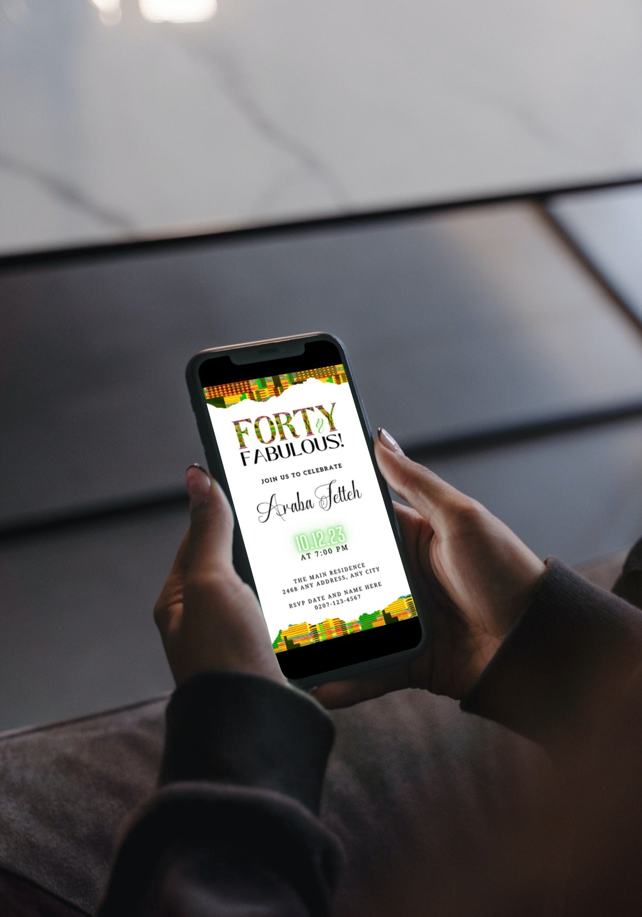 Person holding a cellphone displaying the editable Green Yellow Kente White | 40 & Fabulous Party Evite template from URCordiallyInvited.