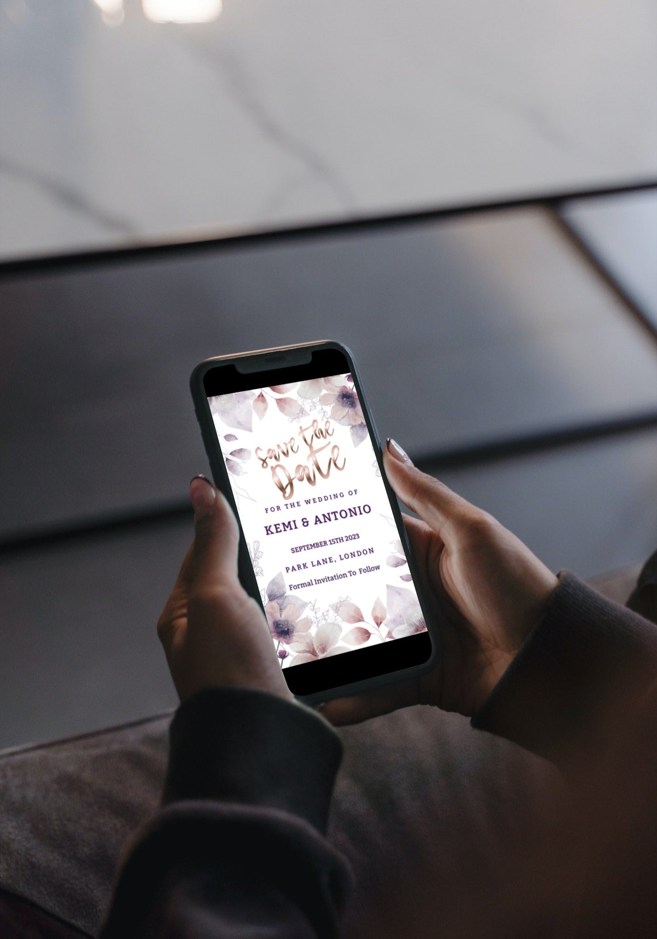 A person holding a smartphone displaying a Boho Rustic Floral Save The Date Evite, customizable via Canva for electronic invitations.
