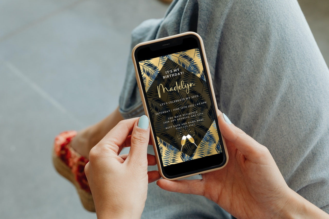 A person holding a smartphone displaying the Gold Blue Tropical Leaf Birthday Party Evite template from URCordiallyInvited.