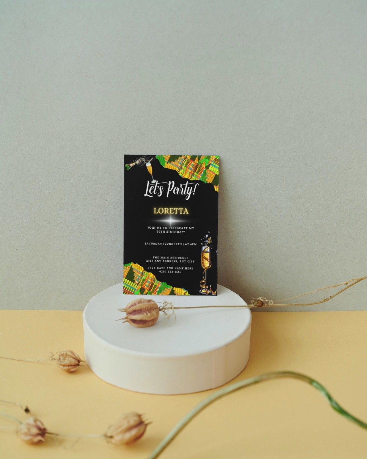 Green Yellow African Kente Editable Birthday Party Evite displayed on a white pedestal, featuring black and yellow invitation elements with a dried flower.