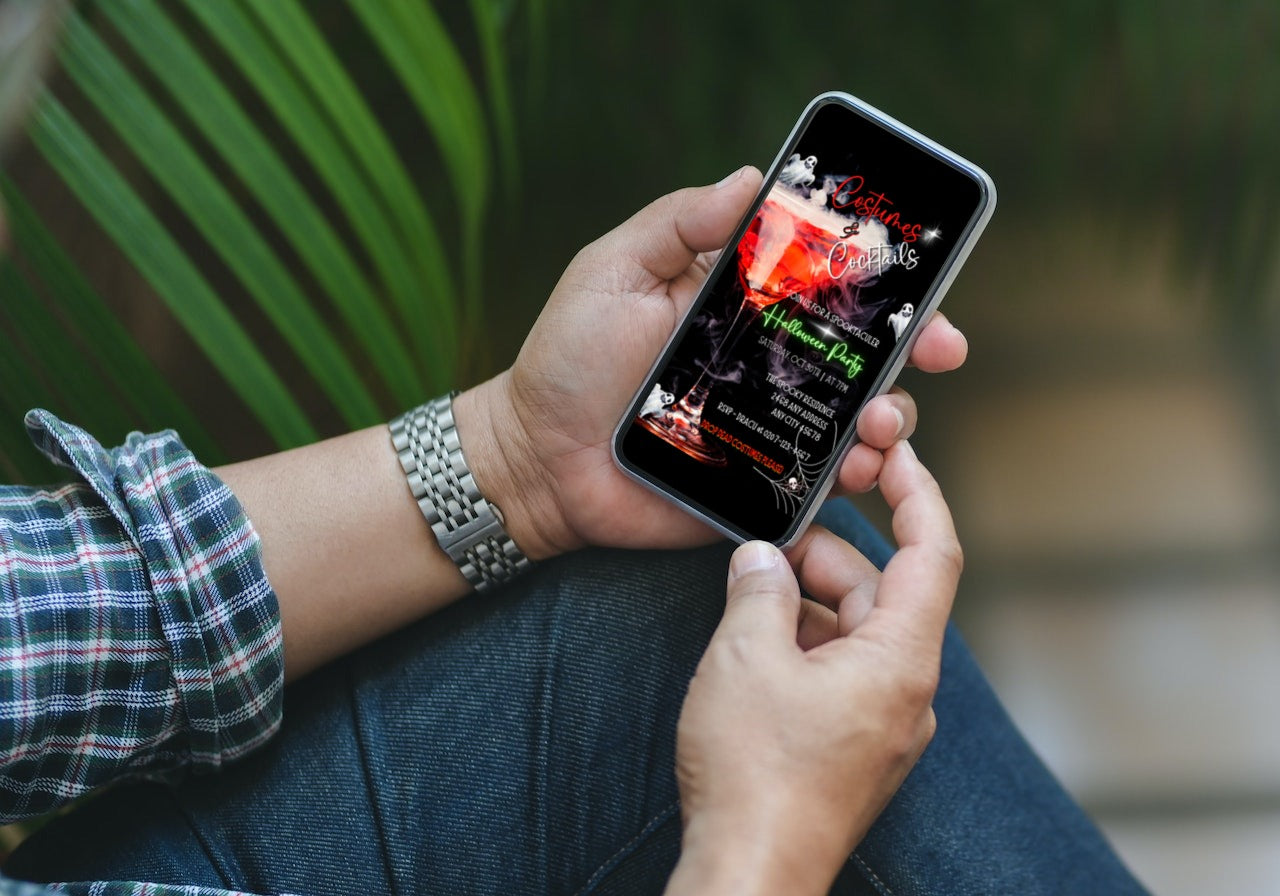 Person holding a cell phone displaying the Smoking Wine Glass Ghosts Costumes & Cocktails | Halloween Evite template, customizable through Canva for digital invitations.