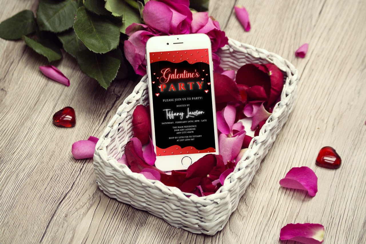 Cellphone in a white basket with pink petals, showcasing the editable Diamond Red Hearts Border Galentines Party Evite.