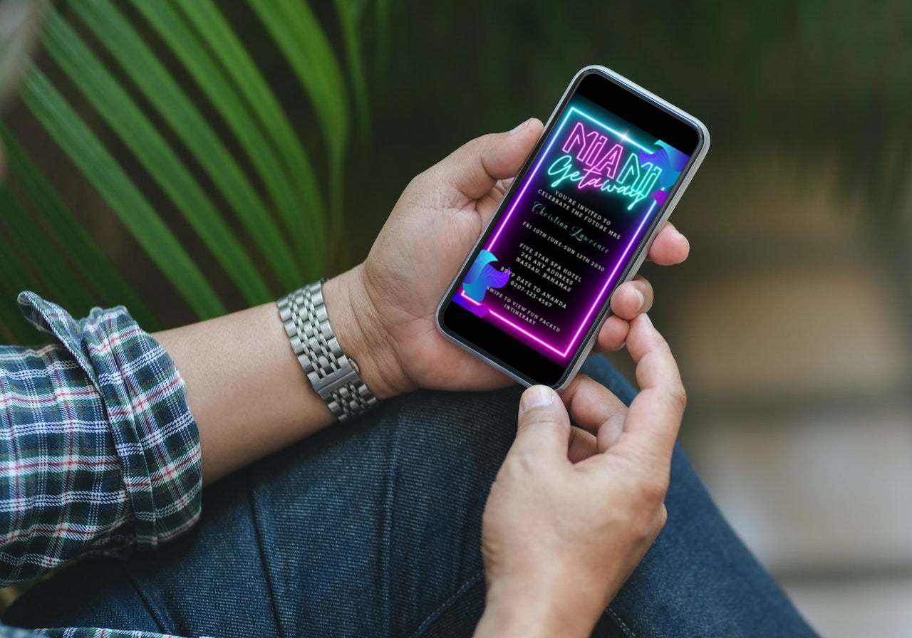 Person holding a smartphone displaying a customizable Miami Teal Pink Neon Getaway Party Evite from URCordiallyInvited, ready for easy personalization with Canva.