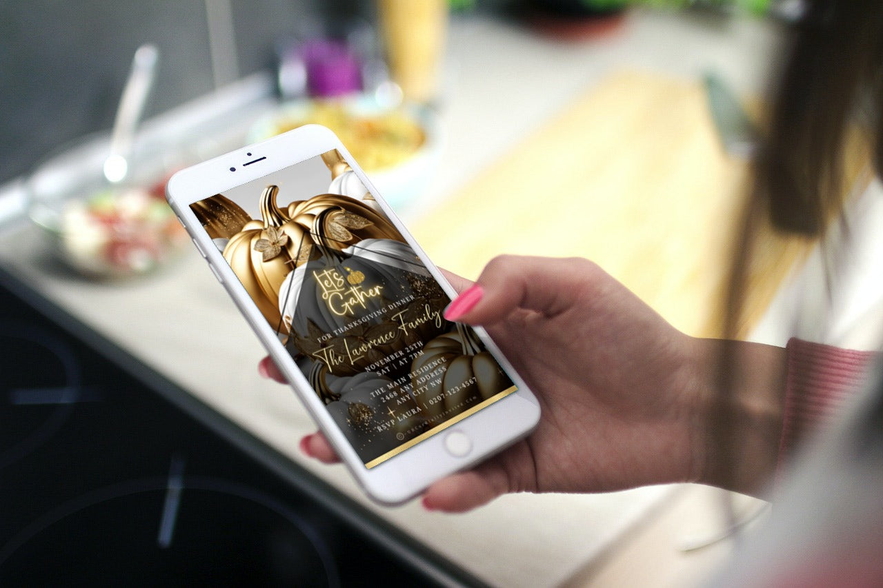 Person holds smartphone displaying Gold Neon White Pumpkin Thanksgiving Dinner Video Invite, showcasing elegant script and festive design over a kitchen countertop.