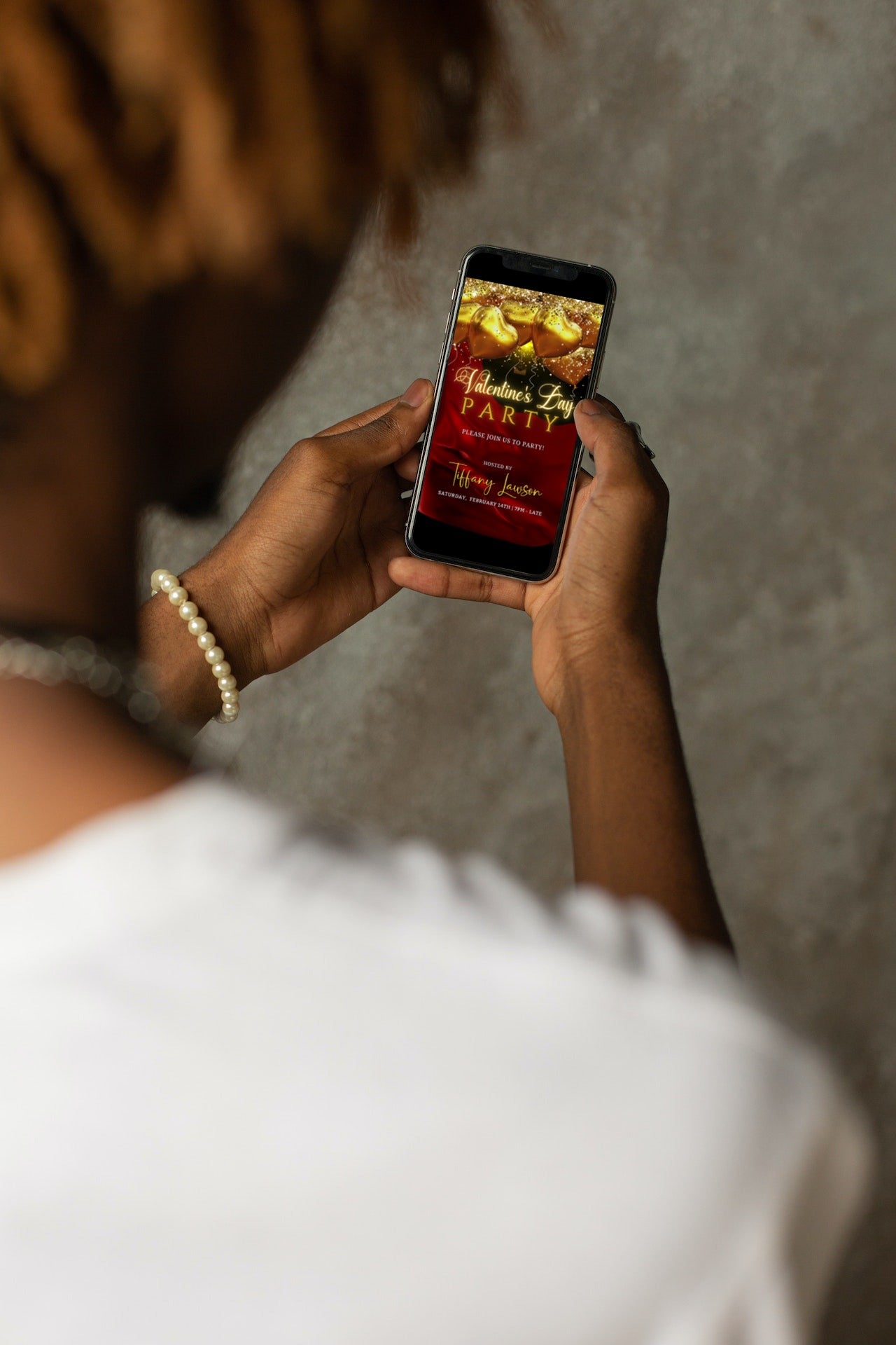 Person holding a smartphone displaying a customizable digital Valentine’s party invite with red silk and neon gold heart balloons.