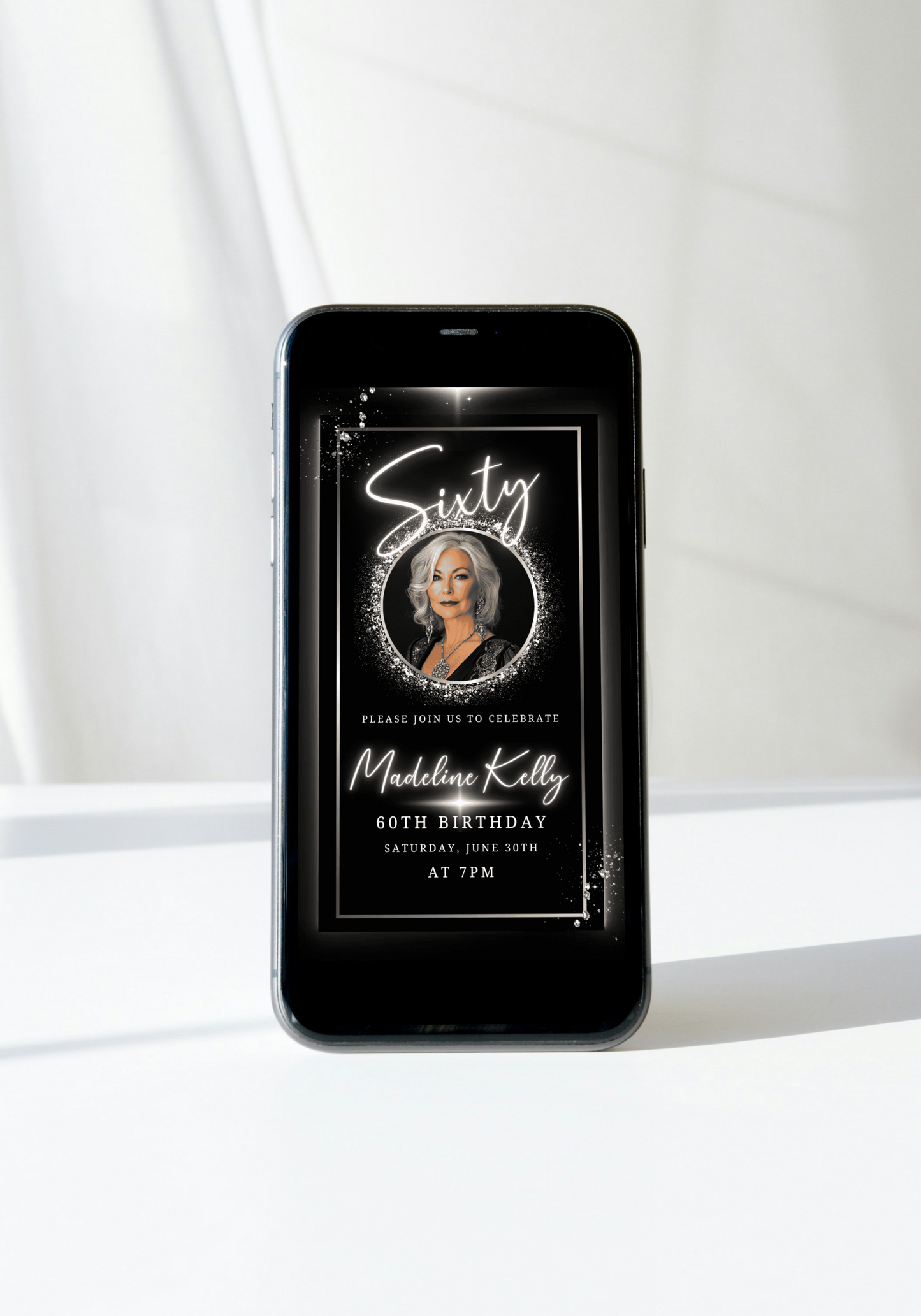 Smartphone displaying the 60th Birthday Video Invitation - Black White Silver Oval Photo Frame Animated Invite, featuring an elegant digital birthday invitation for Madeline Kelly.