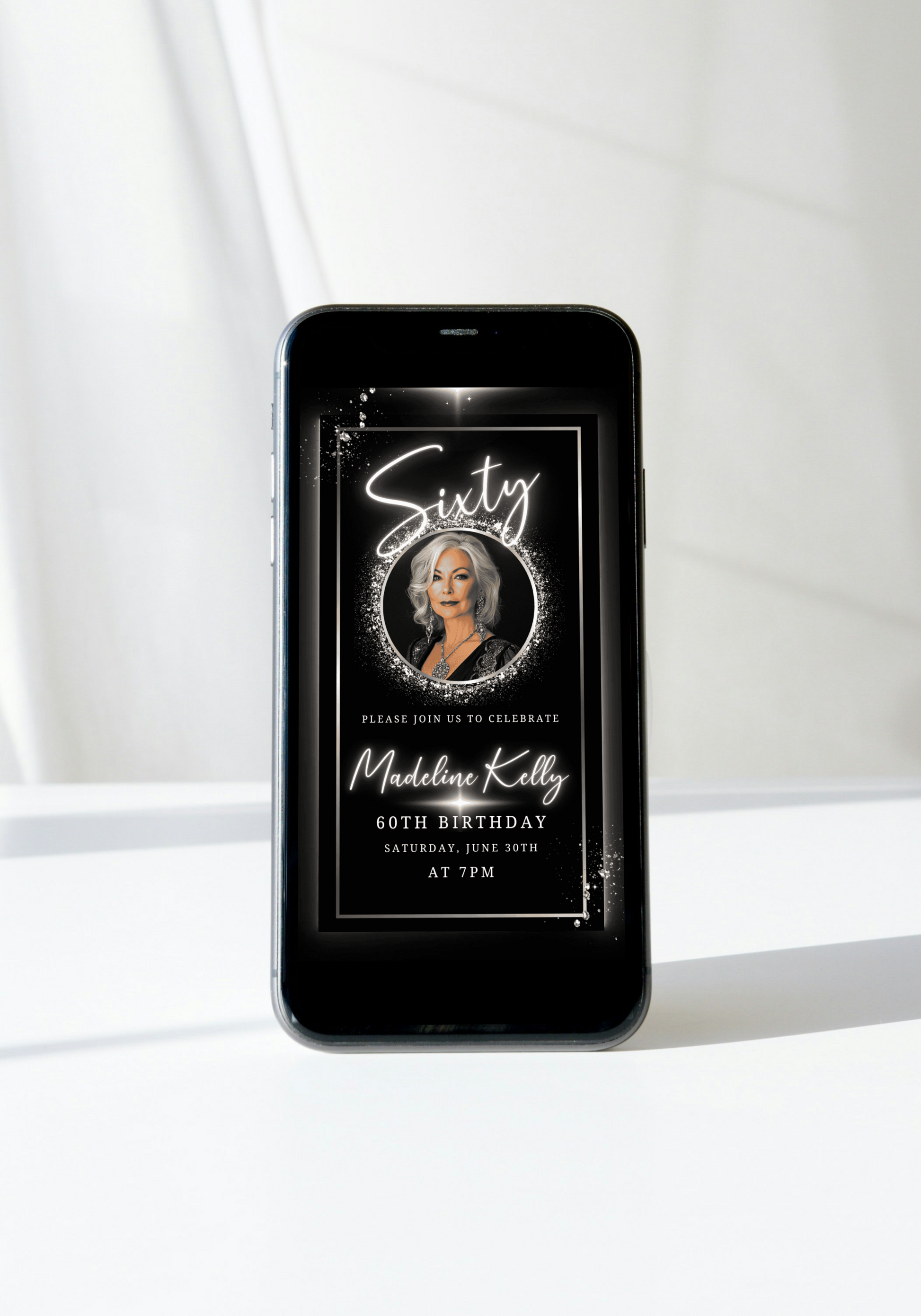 Smartphone displaying the 60th Birthday Video Invitation - Black White Silver Oval Photo Frame Animated Invite, featuring an elegant digital birthday invitation for Madeline Kelly.