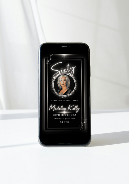 Smartphone displaying the 60th Birthday Video Invitation - Black White Silver Oval Photo Frame Animated Invite, featuring an elegant digital birthday invitation for Madeline Kelly.