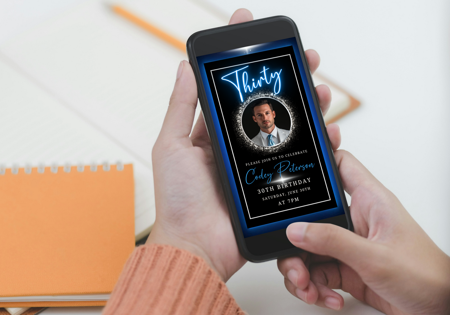 Person holding a phone displaying the Blue & Silver 30th Birthday Video Invitation - Neon Design for Men, showcasing a man's photo in an elegant gold frame.