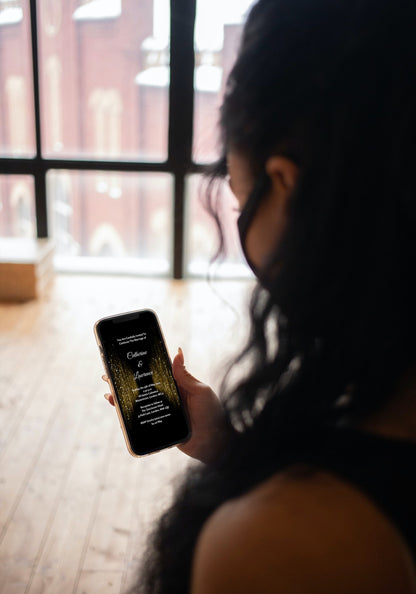 Woman holding a smartphone displaying a customizable Gold Glitter Curtain Wedding Video Invitation template for personalization via Canva.