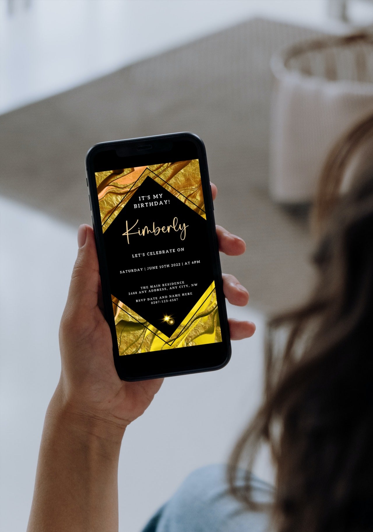 Hand holding a smartphone displaying the Gold Black Ankara Editable Birthday Evite template for customization via Canva.