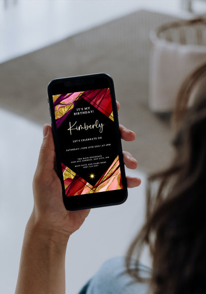 A hand holding a smartphone displaying a Maroon Ankara Themed Editable Birthday Evite template for customization via Canva.