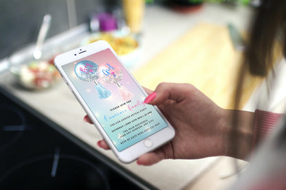 Hand holding a phone displaying a customizable Blue Pink Balloons Sparkle | Gender Reveal Evite template for easy online personalization and sharing.