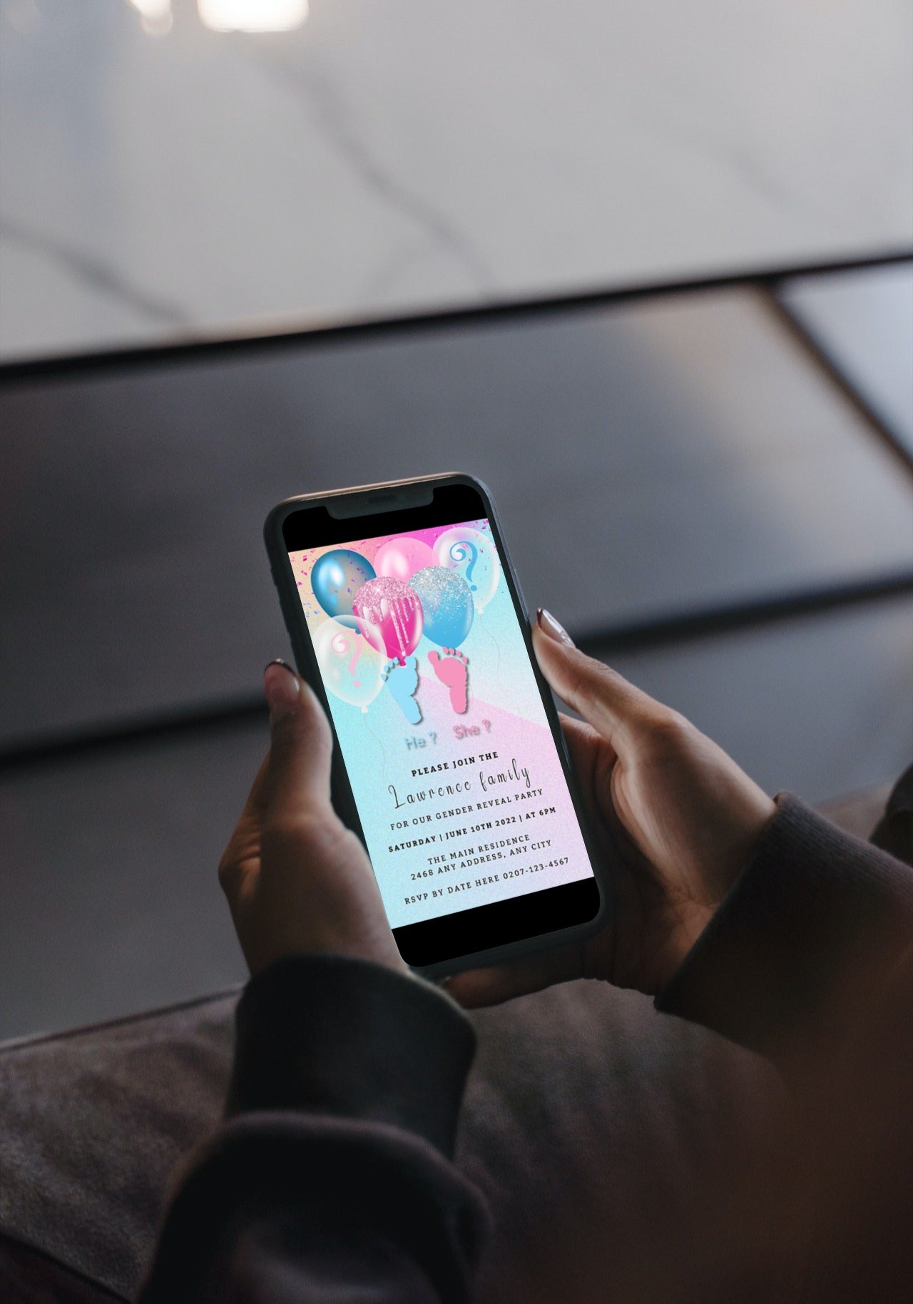 Person holding a smartphone displaying a customizable digital baby shower invitation with floating balloons and baby feet graphics for a gender reveal event.