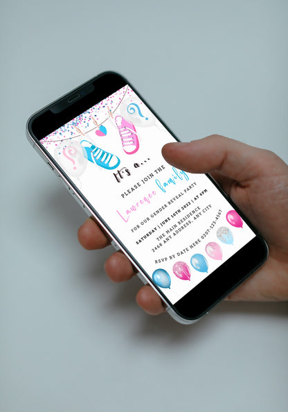 Hand holding a smartphone displaying a customizable digital gender reveal invitation with pink and blue baby shoes.