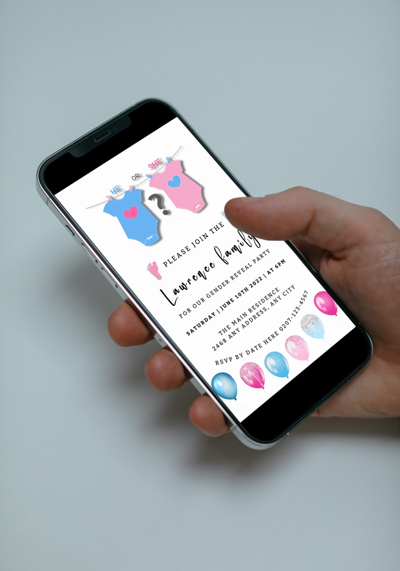 Hand holding a smartphone displaying a customizable digital invitation for a gender reveal, featuring a pink and blue baby grow with a heart design.