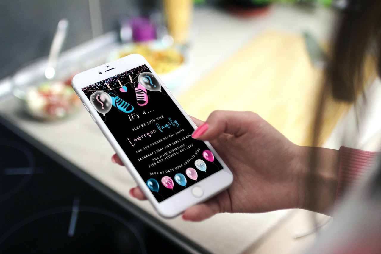 Hand holding a smartphone displaying a customizable digital invitation for a baby gender reveal with black, blue, and pink baby shoes.