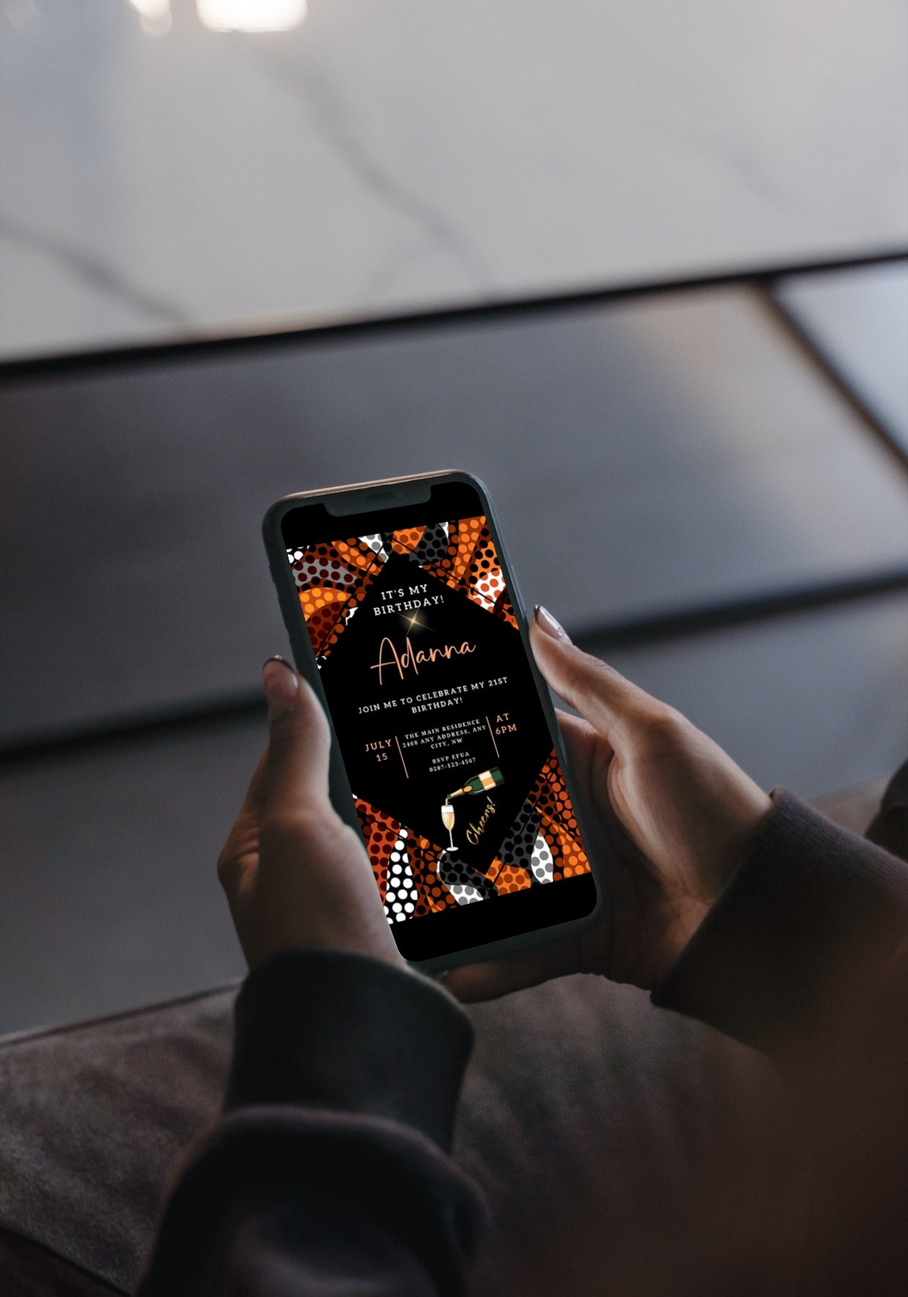 Person holding a cell phone displaying the Orange Black African Ankara Editable Party Evite template from URCordiallyInvited, ready for customization via Canva.