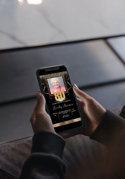 Person holding a smartphone displaying a customizable Black Gold Confetti 80th Birthday Evite with a photo of an elderly woman giving a thumbs up.