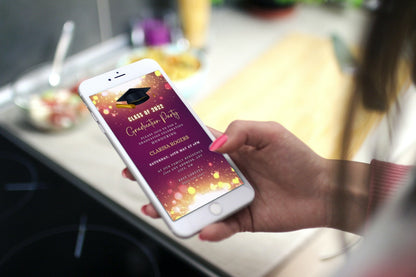 Person holding a smartphone displaying a customizable Maroon Gold Glitter Graduation Video Invitation template from URCordiallyInvited.