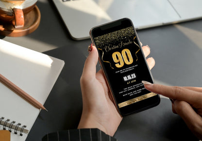 A person holding a phone displaying a customizable Black Gold Confetti 90th Birthday Evite template.