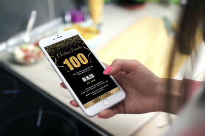 Hand holding a phone displaying a customizable Black Gold Confetti 100th Birthday Evite template with editable text and confetti graphics for digital invitations.