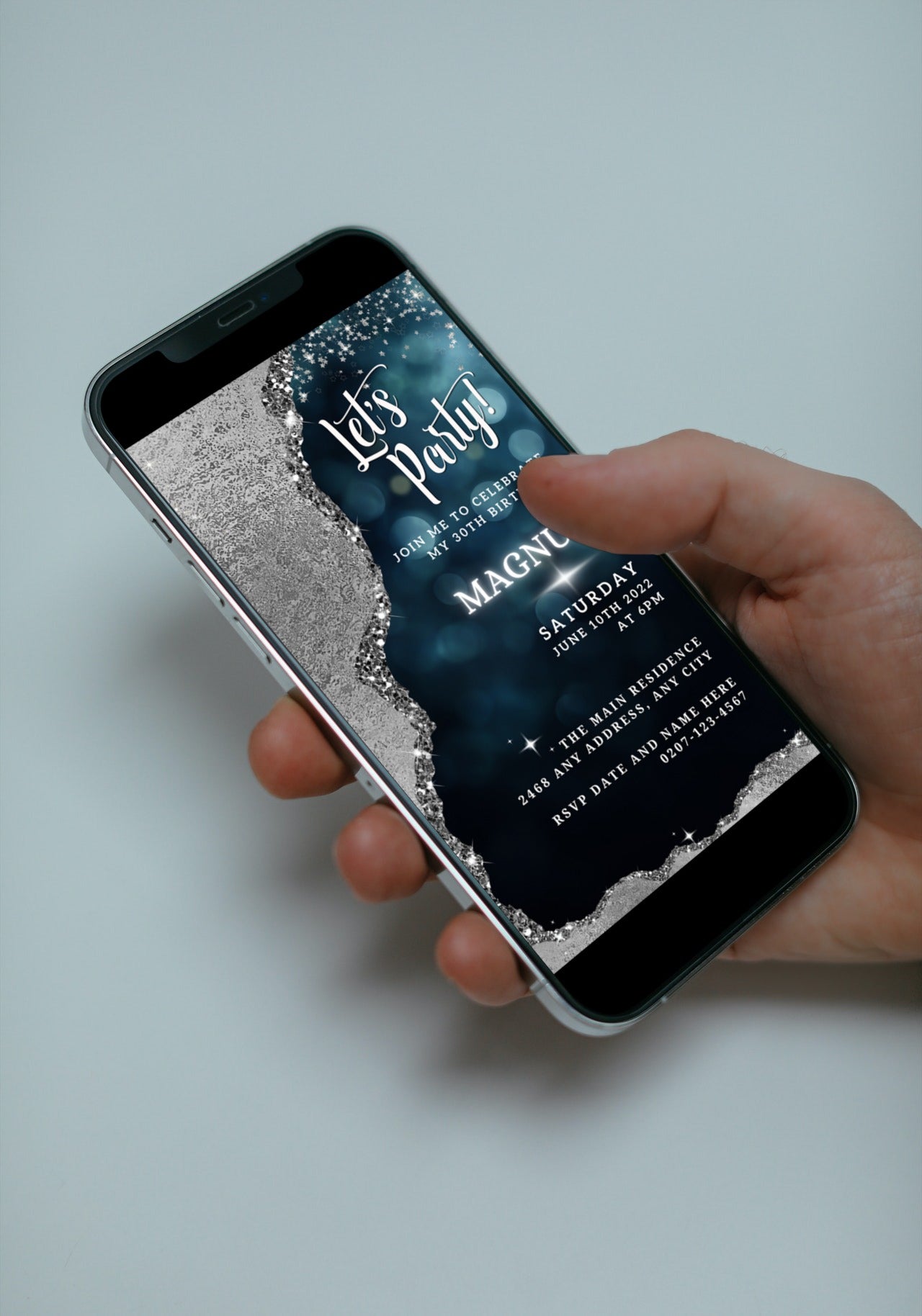 Hand holding a smartphone displaying the Navy Silver Glitter Editable Birthday Evite, a customizable digital invitation template available for download and personalization via the Canva app.