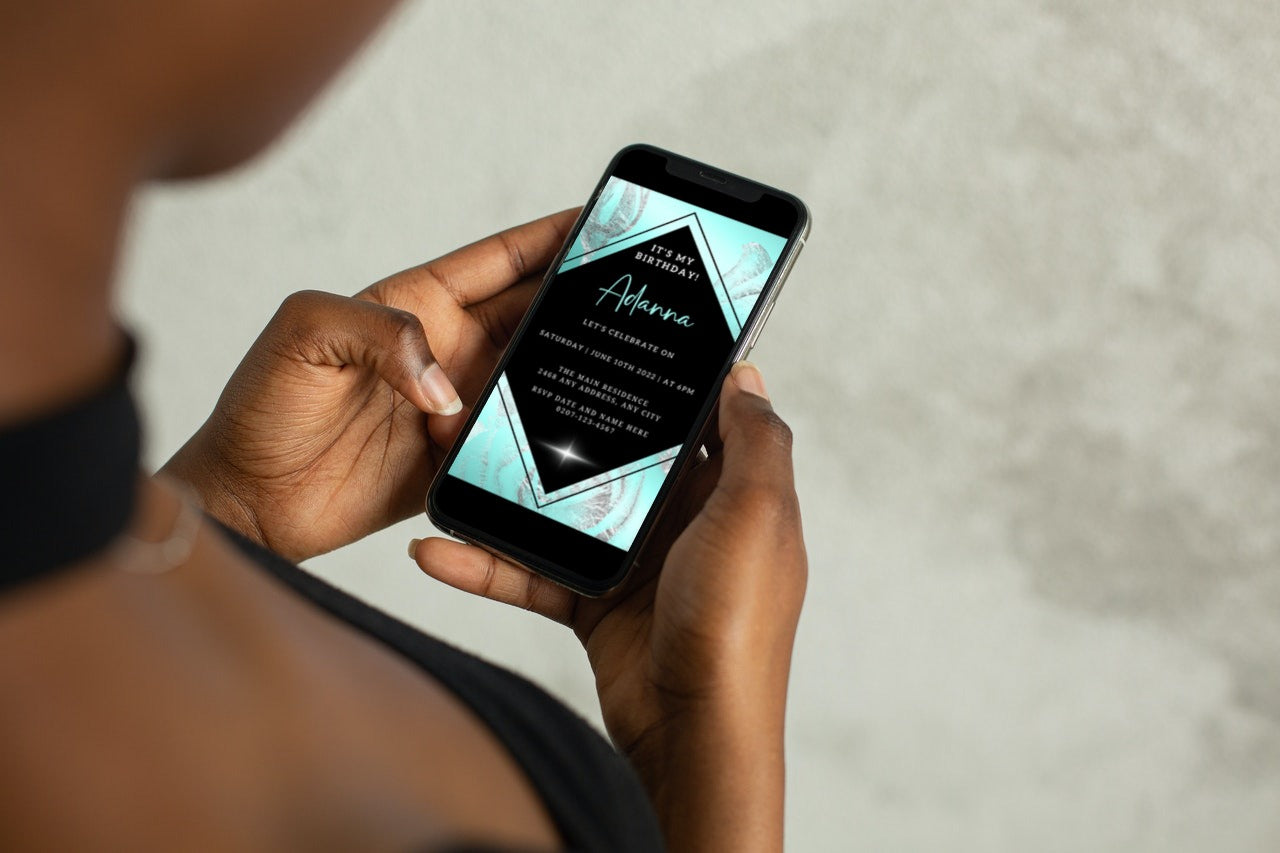 Person holding a smartphone displaying a Teal Black Silver Floral Customisable Birthday Evite from URCordiallyInvited, ready for personalisation via Canva.