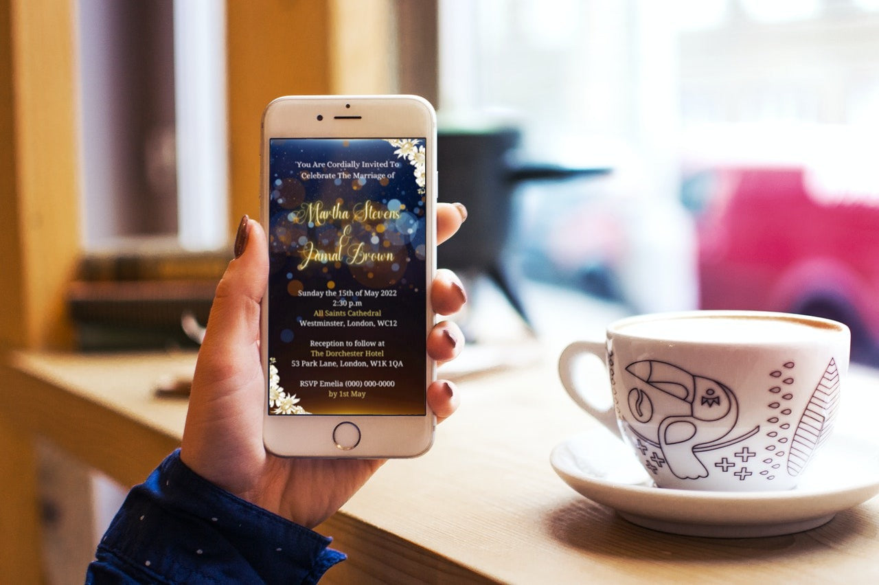 Hand holding a smartphone displaying a customizable Gold Blue Floral Wedding Video Invitation, with a coffee cup nearby.