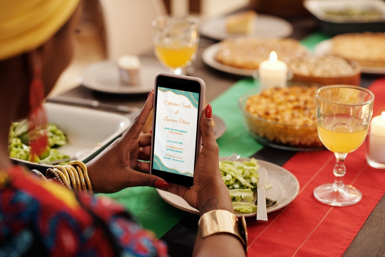 Person holding a smartphone displaying a customizable Teal Blue Agate Wedding Video Invitation template from URCordiallyInvited, with food and drink in the background.