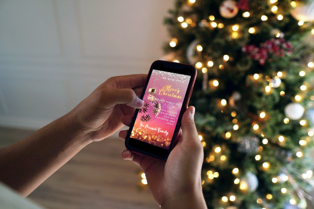 Person holding a smartphone displaying the Fuchsia Gold Ball Glitter Christmas Video Ecard, customizable with Canva for digital invitations.