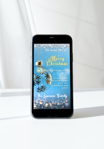 Smartphone displaying a customizable Blue Gold Ball Glitter Christmas Video Ecard template with snowflakes and holiday greeting.