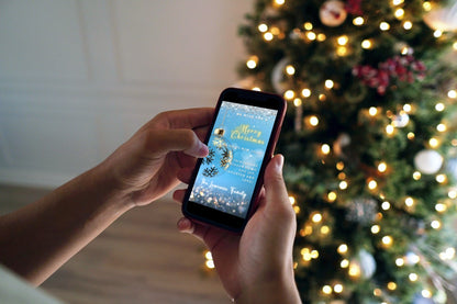 Person holding a smartphone displaying a Blue Gold Ball Glitter Christmas Video Ecard, showcasing URCordiallyInvited's customizable digital invitation template for holiday events.
