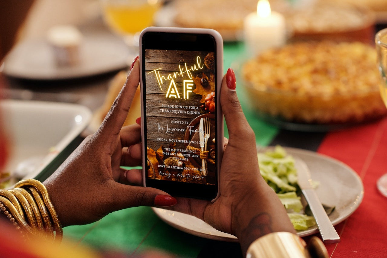 Person holding a phone displaying Thankful AF Neon Wooden Table | Thanksgiving Dinner Evite template, ready to be personalized using Canva.