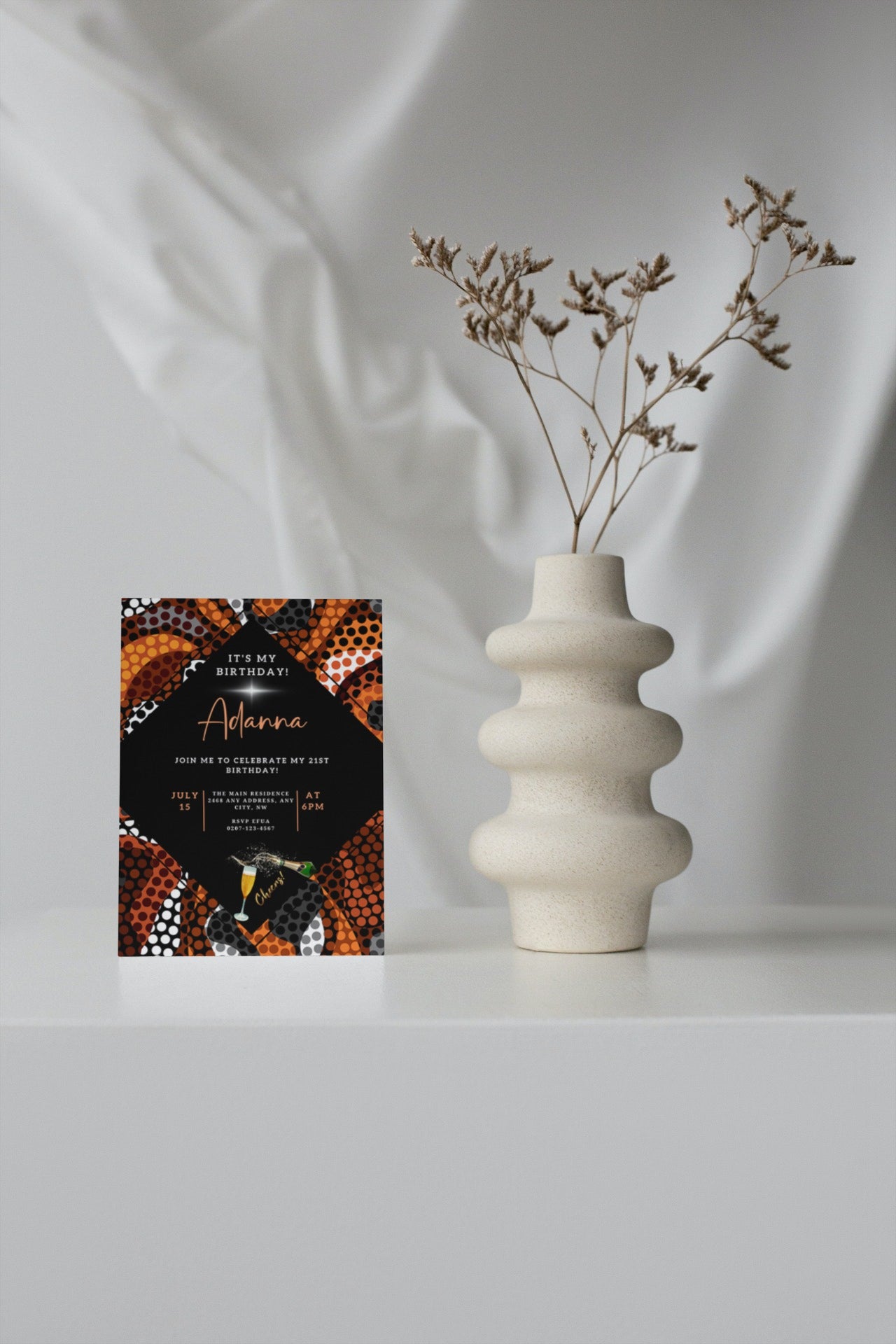 White vase with dried flowers and a card, illustrating the customizable Orange Black African Ankara Editable Party Evite by URCordiallyInvited.