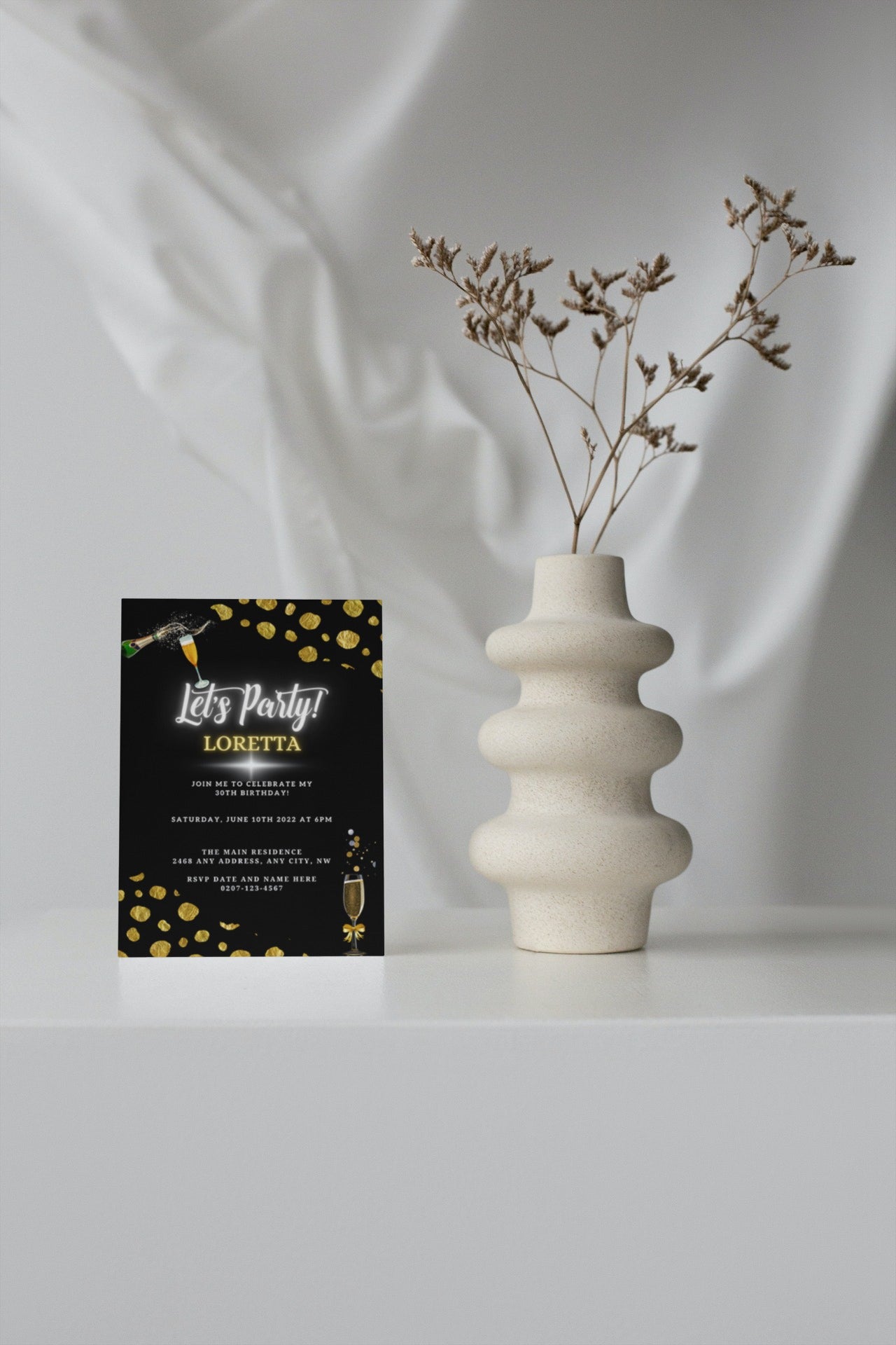 White vase with dried flowers beside a Black Leopard Gold Customisable Party Evite card on a table.