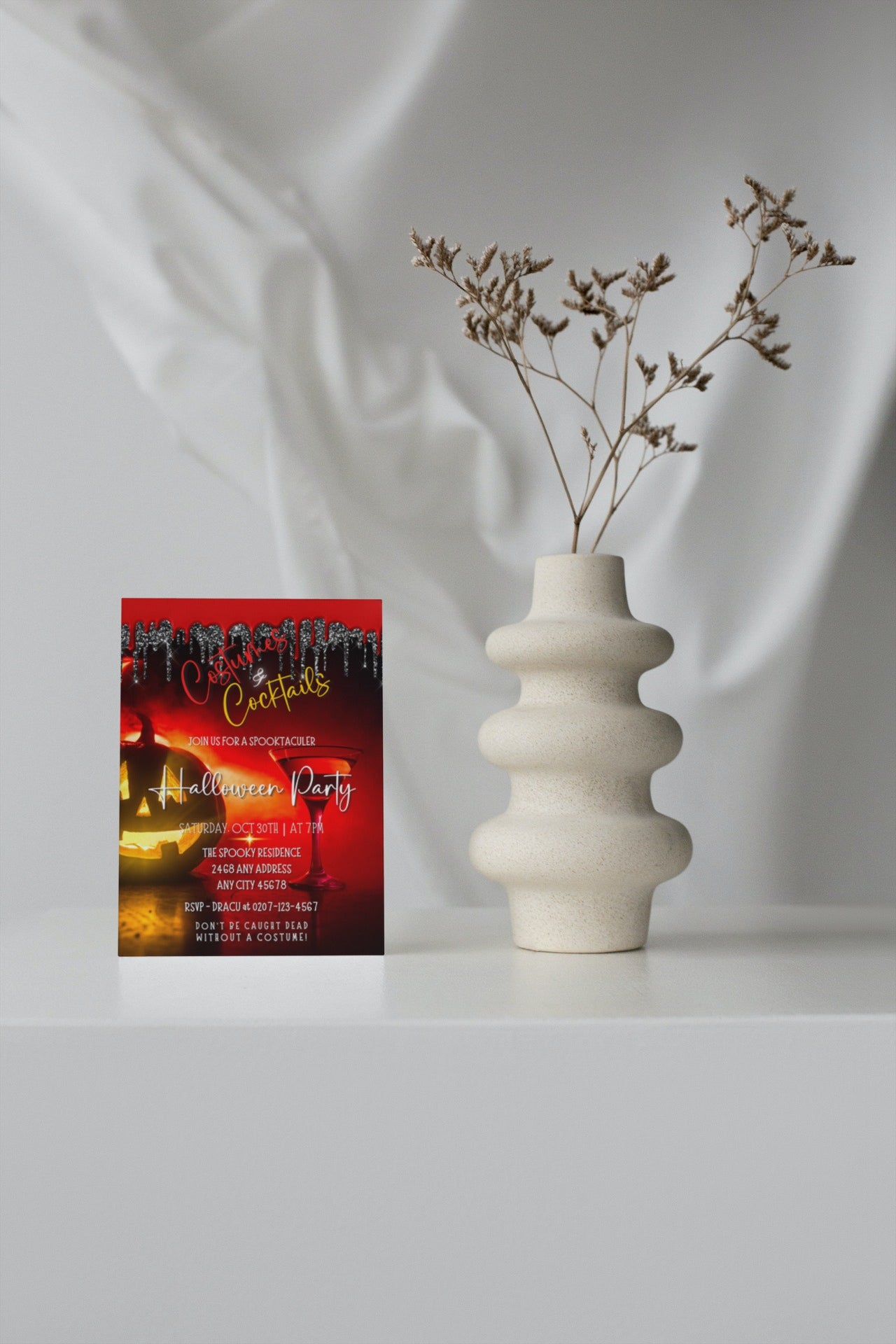 White vase with dried flowers beside a card. Invitation video template for Red Hot Pumpkin Costumes & Cocktails | Halloween Evite available for customization via Canva.