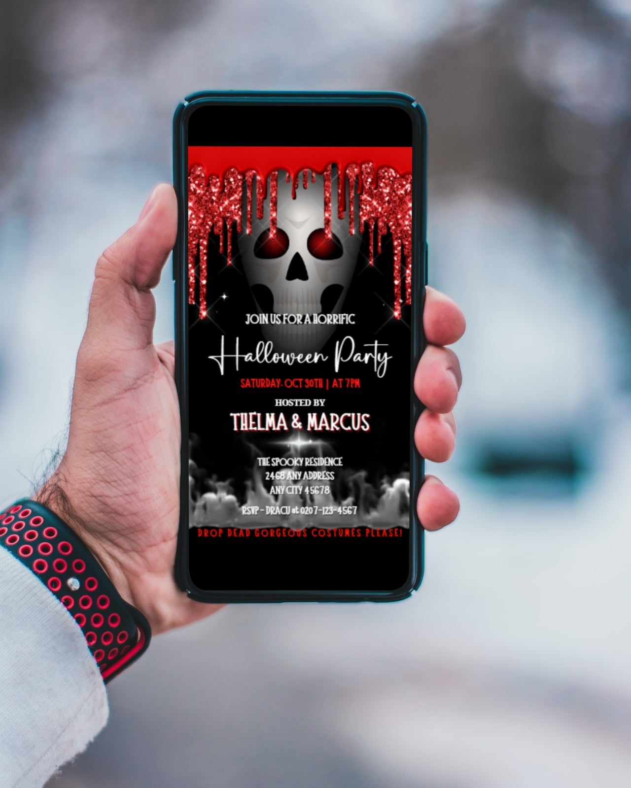 Hand holding a cell phone displaying a digital Halloween party invite featuring a dripping, smoking red-eyed skull.