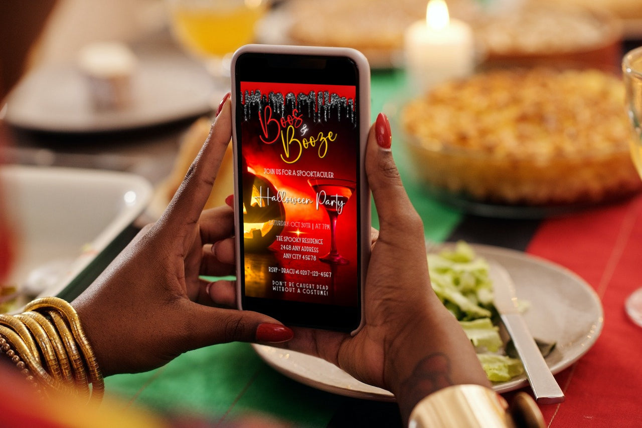 Person holding a mobile phone while viewing the BOOS & BOOZE RED HOT PUMPKIN | HALLOWEEN EVITE customizable digital invitation template on the screen.
