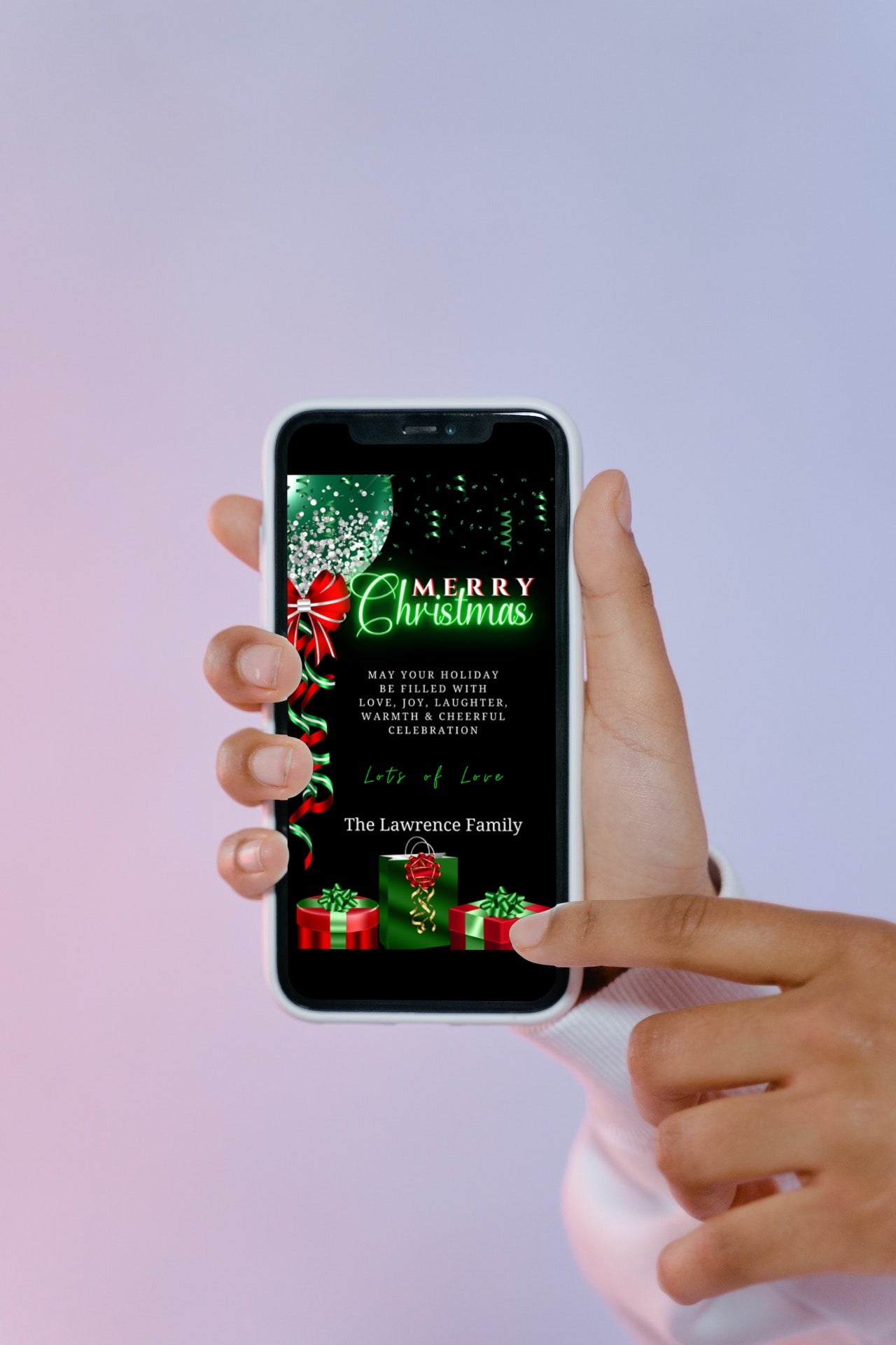 Hand holding a smartphone displaying a customizable Green Neon Presents & Red Green Balloon Merry Christmas Ecard template from URCordiallyInvited.