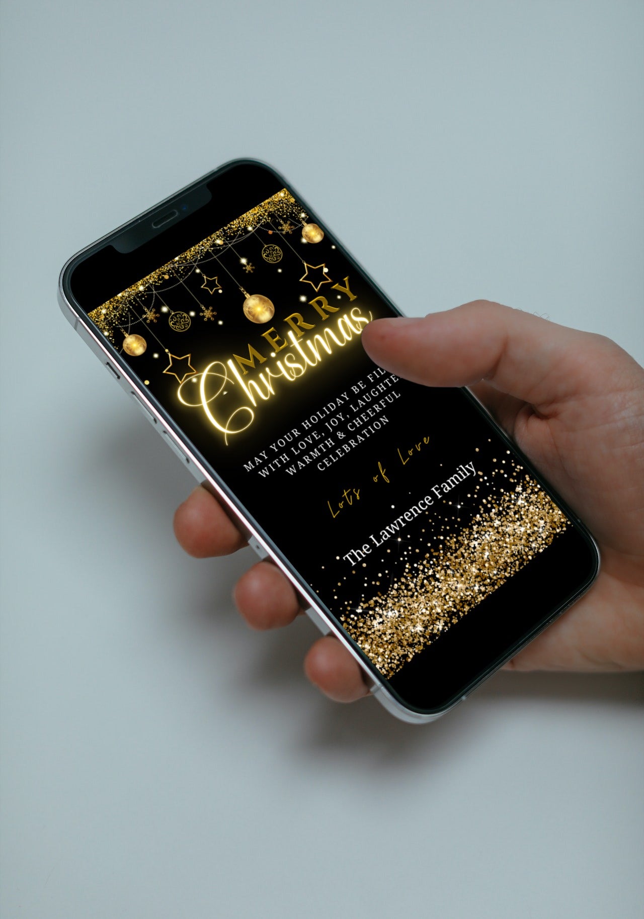 Hand holding a smartphone displaying a customizable Black Gold Ornaments Merry Christmas Greeting Ecard template from URCordiallyInvited.