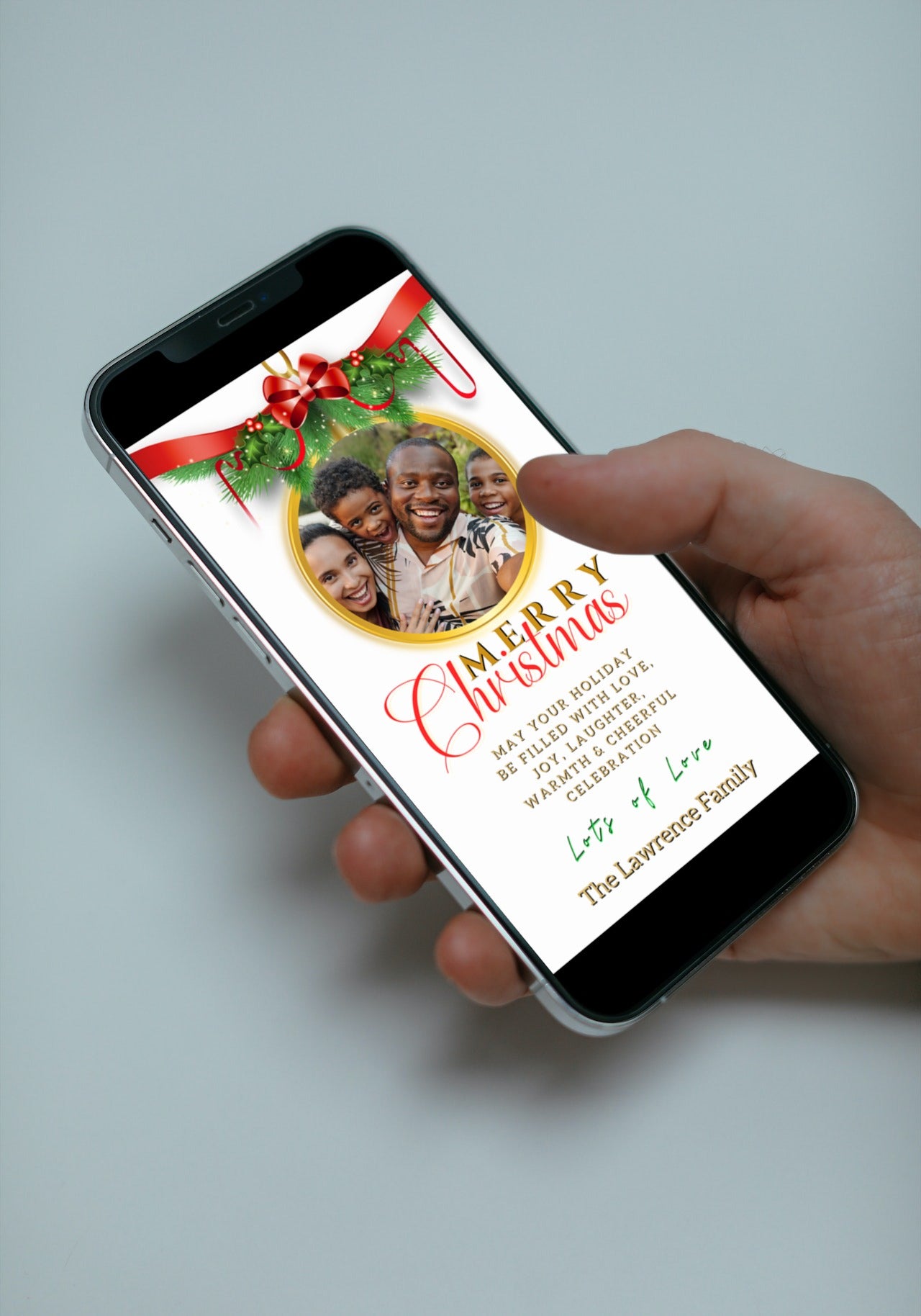 Hand holding a smartphone displaying a customizable Merry Christmas Greeting Ecard with a white red ribbon oval and photo.