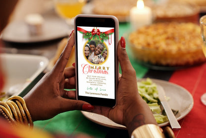Person holding a phone displaying a customizable Merry Christmas Greeting Ecard with a white red ribbon oval design and a family photo.
