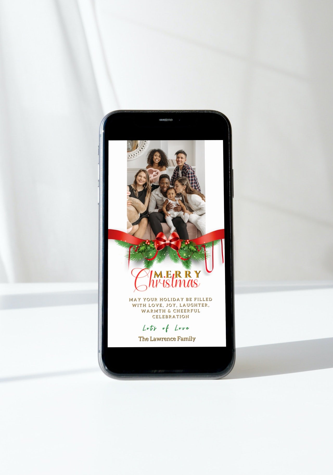 Cell phone displaying a Merry Christmas ecard with a red bow ornament and a family photo.