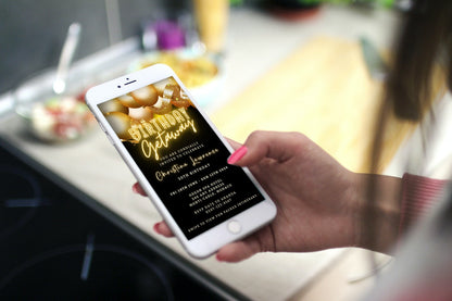 Hand holding a smartphone displaying a customizable Black Neon Gold Balloons | 7 Day Getaway Birthday Evite from URCordiallyInvited.