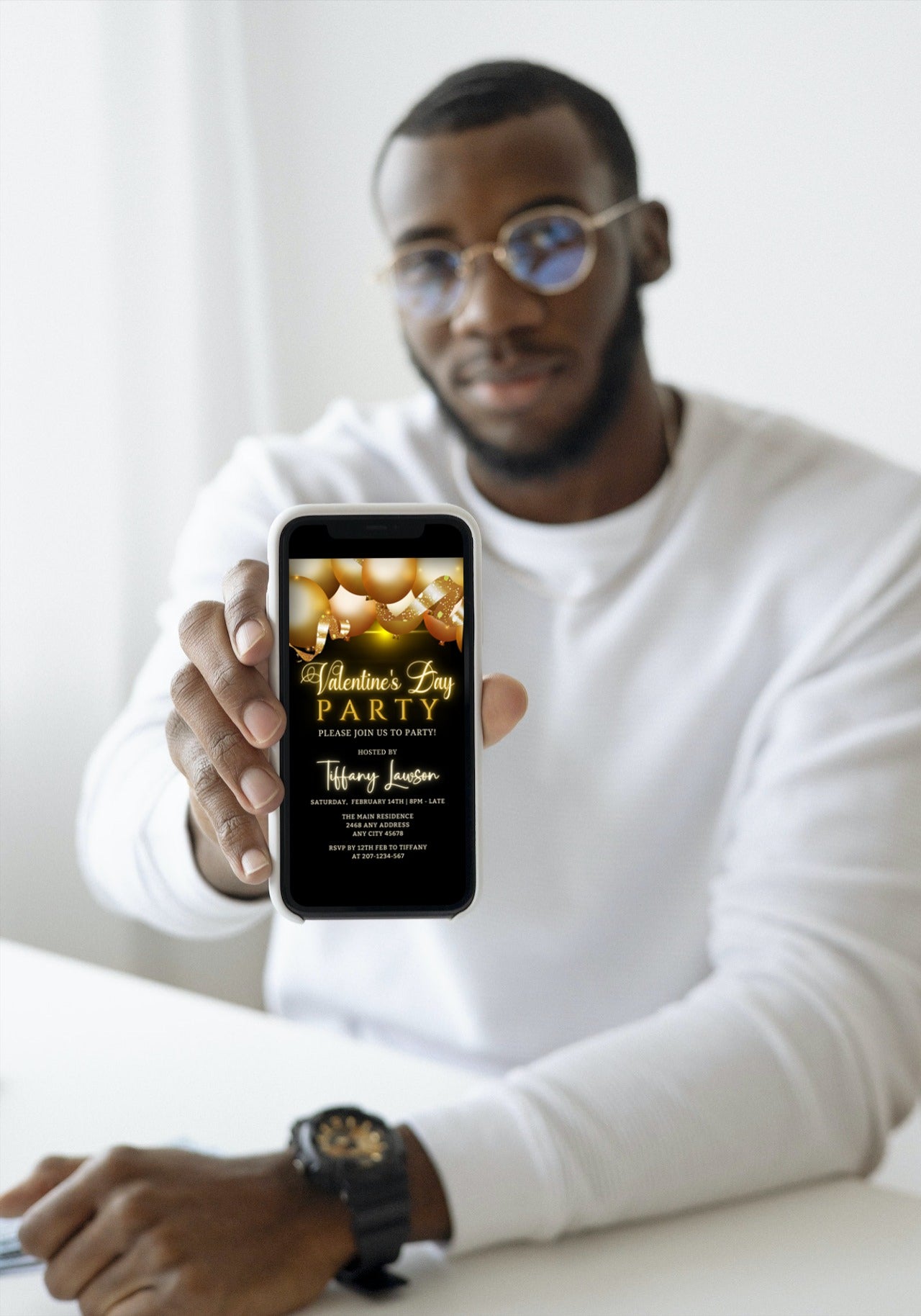 Man holding a smartphone displaying the Editable Digital Black Gold Neon Balloons Valentines Day Party Evite template, ready for personalization and sharing via Canva.