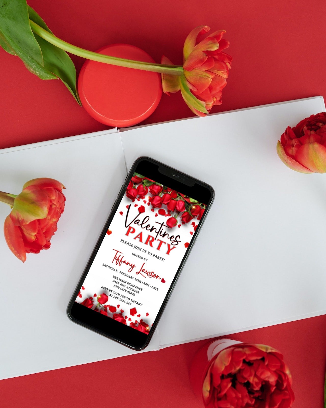 Digital invitation template displayed on a smartphone screen placed on a book, featuring a red roses border theme for Valentine's party.